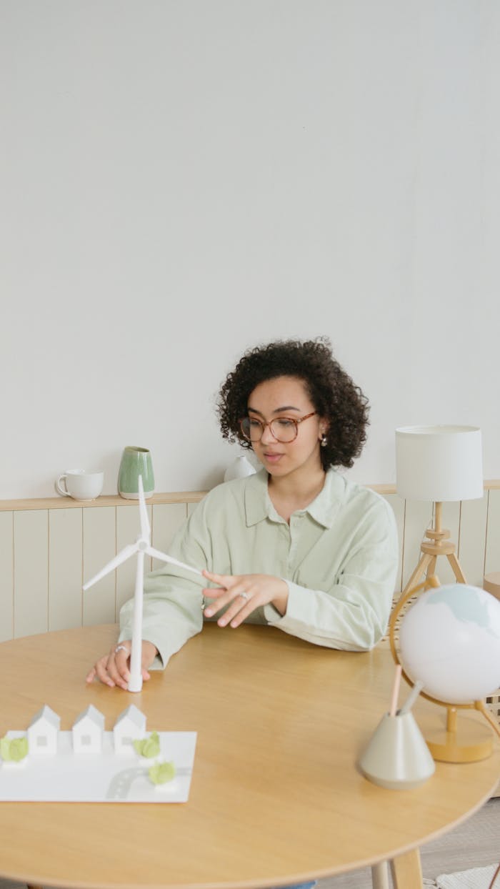 African American woman examining miniature wind turbine at a table, promoting sustainable energy.