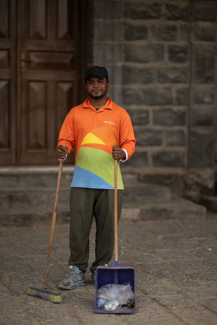 why-choose-us A street sweeper stands with broom and dustpan in front of stone building.