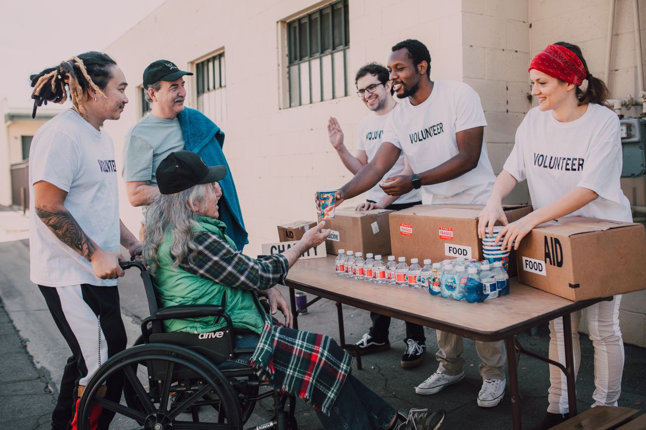 about-01 Volunteers distribute bottled water and supplies to diverse individuals in an outdoor setting, showcasing community support.
